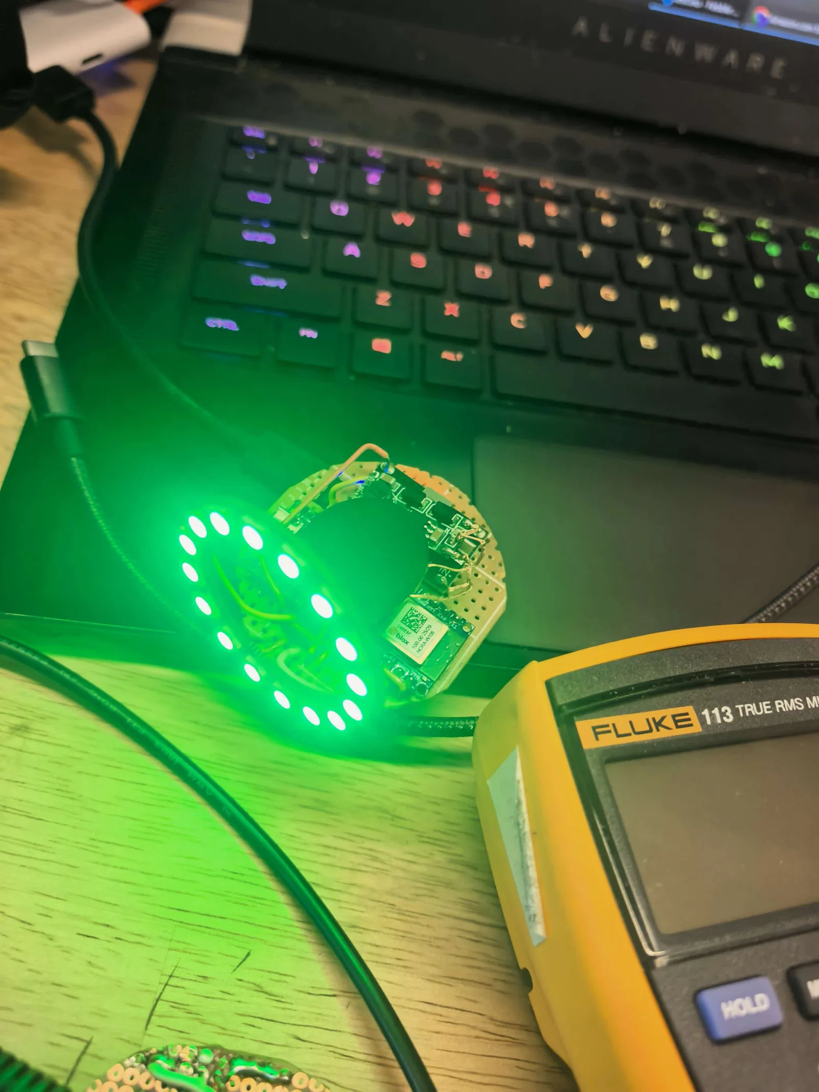 The Pebble prototype glowing green during a bench test next to a multimeter